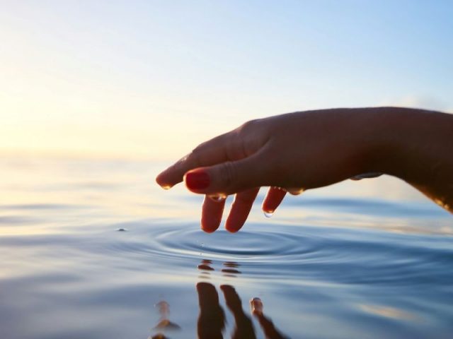 Mão feminina toca o oceano fazendo uma alusão à inteligência emocional e como controlamos a emoção