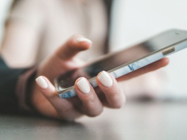 Mão segurando um smartphone com foco no gesto de uso, representando o atendimento profissional via WhatsApp.