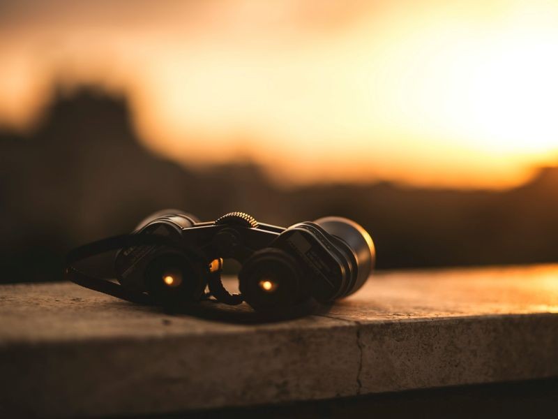 Binóculos apoiados em uma superfície de pedra ao pôr do sol, simbolizando visão de futuro e previsão de vendas com IA.