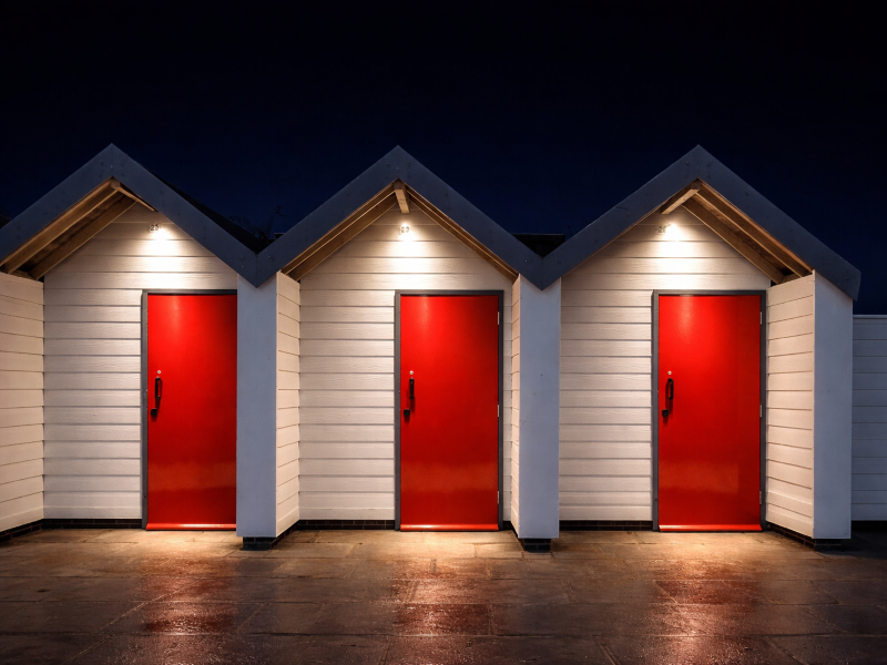 Na imagem, três portas vermelhas de um conjunto de casas brancas que fazem alusão aos 03 erros a serem evitados mencionados neste artigo que fala de IA e CRM.