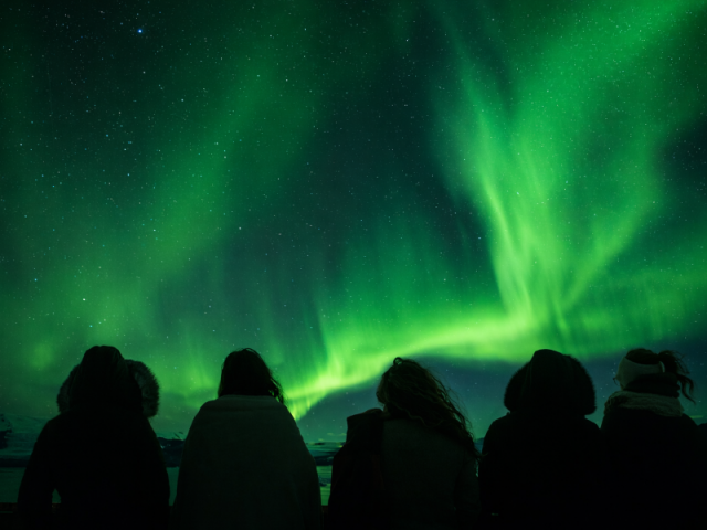 Grupo de pessoas vê a aurora boreal esverdeada. Isso é uma alusão ao uso de grupos no Whatsapp e lista de transmissão