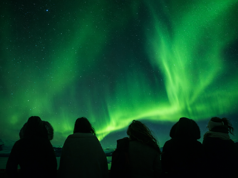 Grupo de pessoas vê a aurora boreal esverdeada. Isso é uma alusão ao uso de grupos no Whatsapp e lista de transmissão